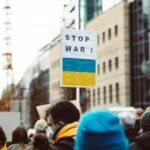 A diverse group of people protesting against war with a focus on a 'Stop War!' sign featuring Ukrainian colors.