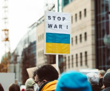 A diverse group of people protesting against war with a focus on a 'Stop War!' sign featuring Ukrainian colors.