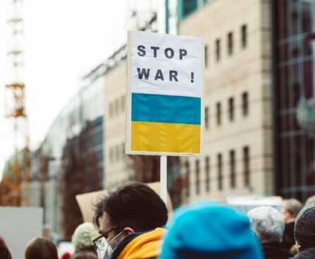 A diverse group of people protesting against war with a focus on a 'Stop War!' sign featuring Ukrainian colors.